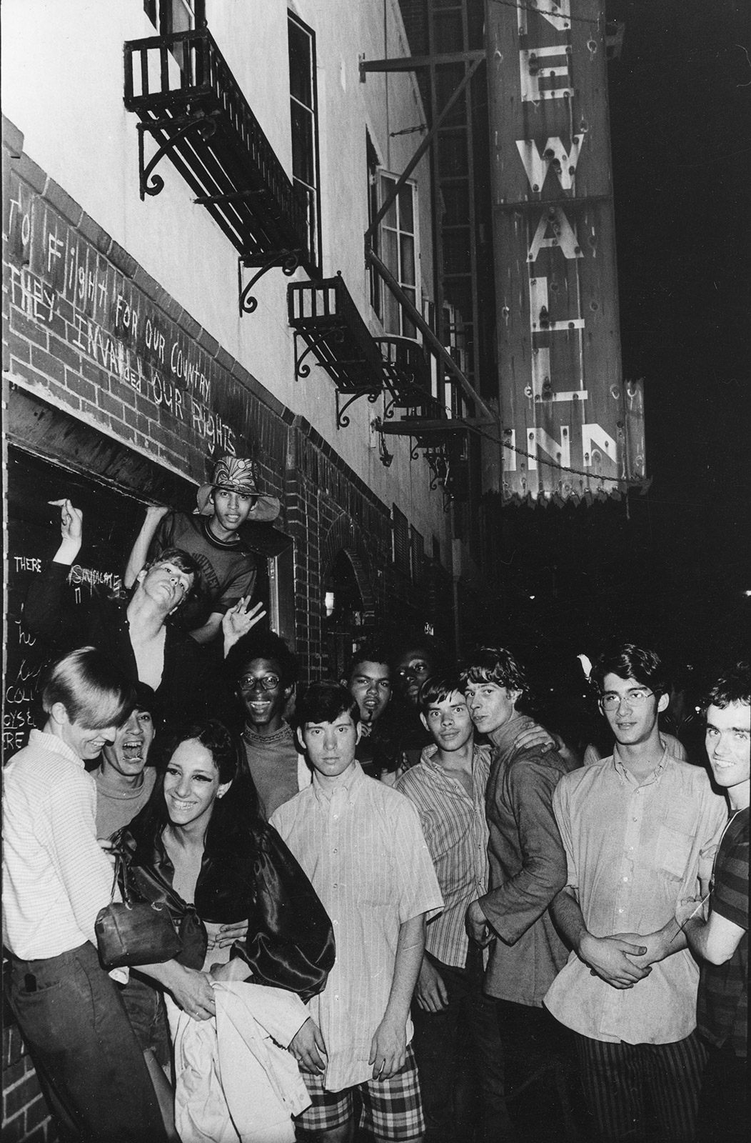 A crowd gathers outside the Stonewall Inn beside graffiti protesting the raid