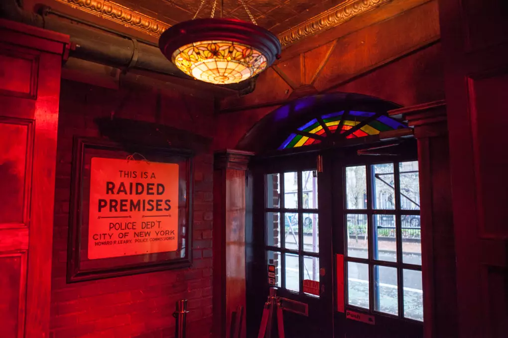 The Stonewall Inn entrance, with a framed This Is a Raided Premises police sign beside rainbow stained glass doors